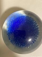 Close-up photo of the clear glass paperweight with a deep blue center and many small air bubbles inside, arranged in a circular pattern.