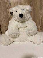 Large white plush bear sitting against wooden backdrop