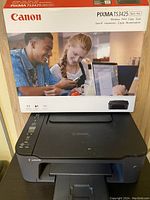 Canon PIXMA TS3425 printer resting on table with original box placed on top. Box shows model, features, and branding.