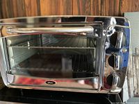 Front view of Oster toaster oven showing stainless steel exterior, glass door, and three control knobs.