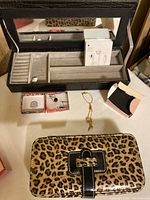 Open black leather travelling jewellery case with compartments and a mirror, leopard print pouch, box of white earbuds, Avon chain and onyx earrings in Royal Voices boxes