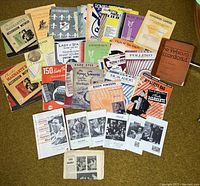 Full view of collection of vintage accordion sheet music and instructional books laid out on carpet.