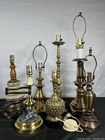Full view of seven brass and glass lamps of varying heights and designs, arranged on black surface against white background.