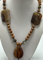 Full view of necklace displayed on bust showing chocolate Tahitian pearls and amber-toned ammolite cabochon gemstones in rectangular and teardrop shapes.