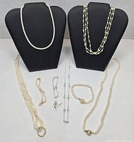Full lot overview showing two black busts with pearl necklaces and eight pearl jewelry pieces laid out: five necklaces and two bracelets, plus earrings.