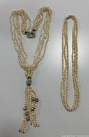 Two vintage freshwater pearl necklaces laid flat showing the multi-strand design with ornate tassel and simpler three-strand necklace.