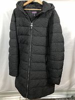 Full front view of the black quilted Long Tall Sally winter coat hanging on a hanger, showing texture and zipper closure.