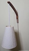 Unlit lamp showing teak wood arm, white cord and conical fabric shade