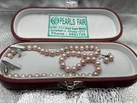 Necklace and earrings displayed in red leatherette case with white lining and green ‘Pearls Fair’ label
