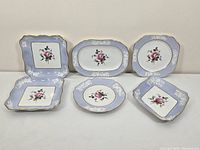 All six Spode Maritime Rose serving plates arranged showing rectangular, diamond, round, and square shapes with blue borders, white floral patterns, and central pink rose.