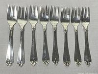 Eight salad forks arranged side by side on gray fabric background