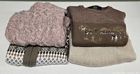 Three folded sweaters, showing colors and knit patterns including brown with hunting dog embroidery.