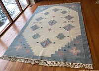 Full view of rug on hardwood floor showing overall geometric medallion pattern and fringed edges