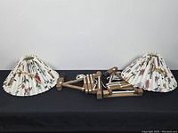 Two folded lamps and two detached shades on black cloth backdrop