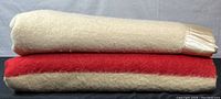 Two folded wool blankets stacked, cream blanket atop Hudson’s Bay blanket showing cream and red stripe.
