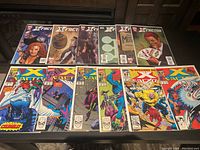 Photo showing all 12 Marvel X-Factor comic books laid out in two rows on a black surface, displaying their colorful covers with various characters and scenes from vintage to modern issues.