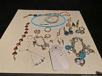 Various costume jewelry items displayed on a beige surface including necklaces, bracelets, rings, earrings, and pendants.