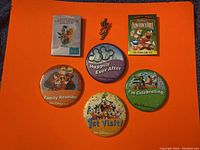 Photo showing all 6 Disney button pins and the small Mickey Mouse lapel pin on a dark cloth background