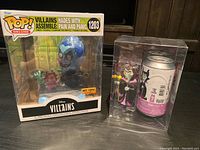 Photo showing Funko Pop Deluxe Hades with Pain and Panic, and Maleficent Funko Soda figure with can in case.