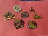 Seven Disney themed trading pins arranged on a red background showing various characters and designs.