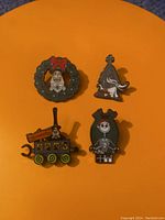 Four enamel lapel pins from the Nightmare Before Christmas collection arranged on an orange background.