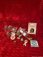Photo of all 16 lapel pins and one keychain laid out on red textured fabric.