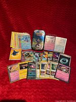 Overview of all Pokémon cards laid out with tin and lapel pin on red fabric background.