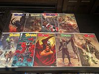Photo of 9 Spawn comic books arranged in 2 rows displaying front covers with a variety of art styles and characters.