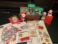 Photo showing all lot items arranged on a surface including boxed candle holders, figurines, boxed Avon candle, fabric tree skirt, and various Christmas-themed paper decorations.