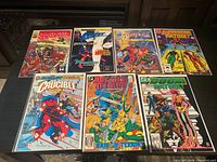 Seven vintage comic books laid out on a table with full front covers visible. Titles include Sequisha, Phantom Stranger, Strangers, Justice League International, Crucible, Bodyguard, and Deadly Nightshade.