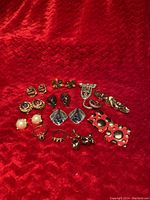 Photo shows an assortment of vintage costume jewelry laid out on red chevron fabric including earrings, rings, and brooch clips.