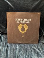 Front cover of the Jesus Christ Superstar vinyl record album, brown background with white text and gold emblem.