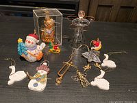 Photo showing assortment of 12 vintage Christmas ornaments on a black surface, includes a variety of shapes and materials such as glass, plastic, and fabric