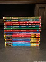 Overview photo showing spines of fifteen Goosebumps books by R.L. Stine with colorful titles and R.L. Stine author name. Books are first editions and apple fiction imprint.