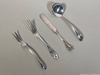 Four sterling silver serving utensils arranged on a flat surface, showing different styles and details