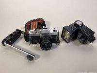 Camera, flash, flash bracket and fabric strap arranged on white surface.