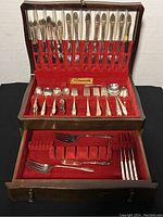 Full view of the open wooden chest displaying the silver plated flatware set with red velvet lining.