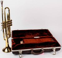 1967 Olds Ambassador trumpet standing next to open hard case with red velvet interior lining and accessory compartment.