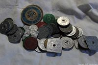 Photo showing a large pile of assorted tax tokens in various shapes, colors, and sizes scattered on a white surface.