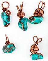 Five Kingman turquoise pendants with copper wire wrapping arranged on white background showcasing shape and wire details