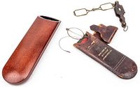 Brown textured hard case, leather pouch embossed B. Pike Jr., and wire rim folding glasses shown together.