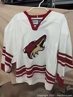 White CCM Arizona Coyotes hockey jersey with maroon and tan logo and stripes, size M, shown on hanger.