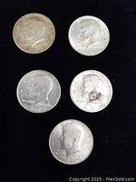 Obverse sides of five Kennedy half dollar coins showing dates 1964, 1971, 1972, and two 1976 coins, one with dark discoloration.