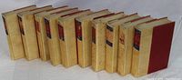 Image of 11 hardcover books with beige and red covers arranged in a slight diagonal line, showing spine details.
