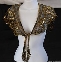 Front view of the black sheer evening shawl with gold bead and sequin decoration, tied at front with tassels.