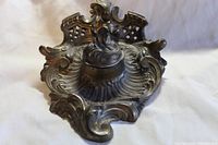 Front angled view of the brass ornate ink well holder showing lid closed, decorative base with scrolling and lattice work.