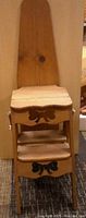 Front view of wooden ironing board/chair showcasing bow cutout decoration on the front panel below the seat and on lower support.