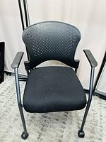 Front view of black office chair showing perforated backrest, fabric seat, armrests and wheels.