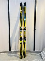 Full view of the pair of yellow Head Cyber skis with bindings displayed upright.