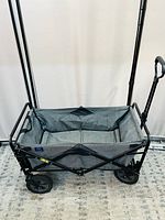 Side view of the utility wagon showing black metal frame, gray fabric bed, wheels, and pull handle